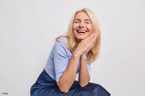 Mature woman with blonde hair laughing with her head resting on her hands